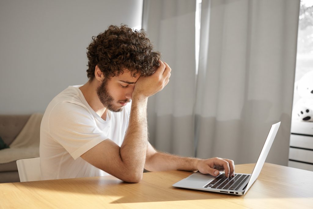 picture tired young male translator with thick beard wavy hair touching head closing eyes feeling absolutely exhausted keyboarding laptop translating technical documentation